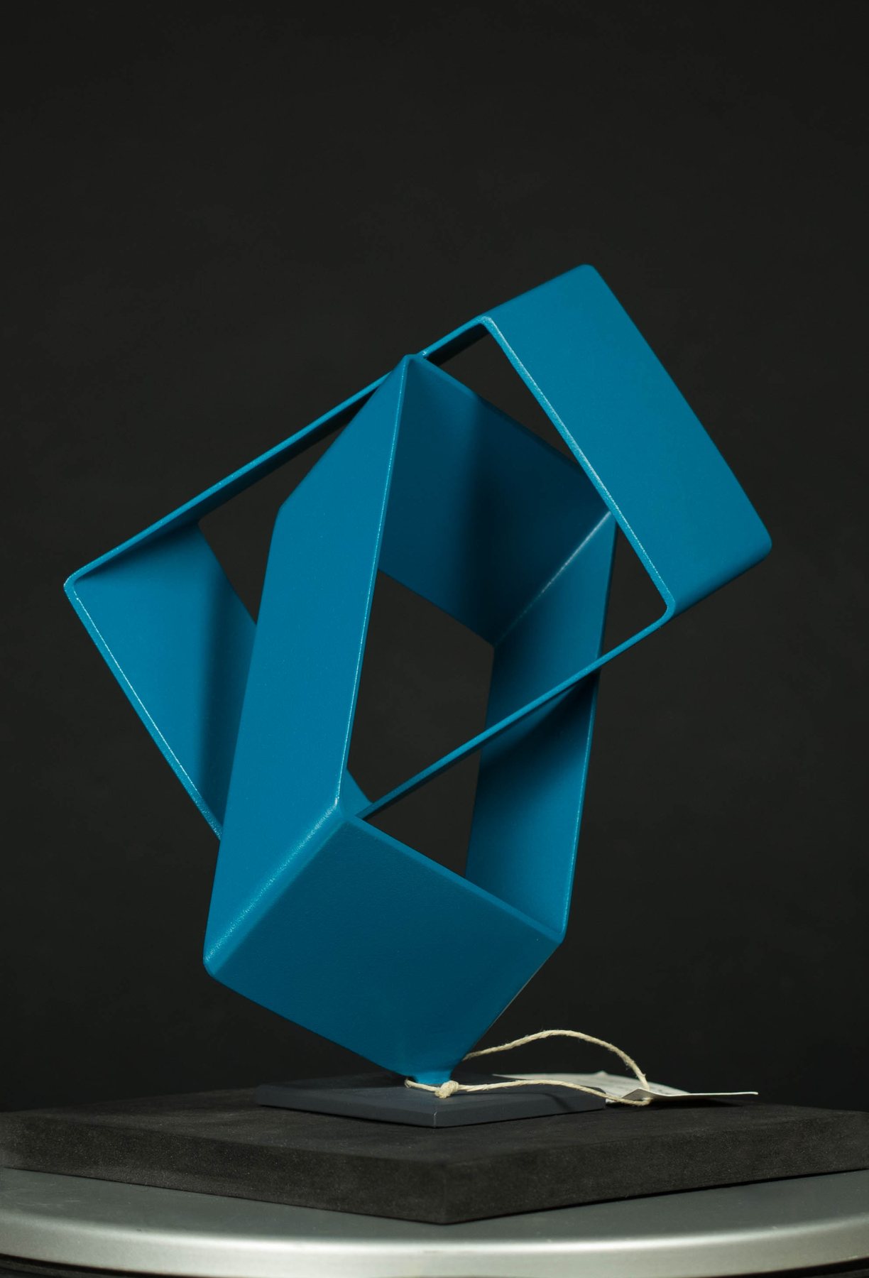 Escultura geométrica azul de formas entrelazadas, sobre pedestal