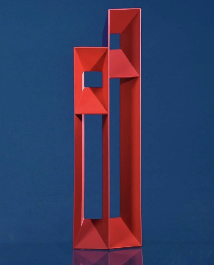Dos esculturas verticales de la serie Personas, en rojo, sobre fondo azul
