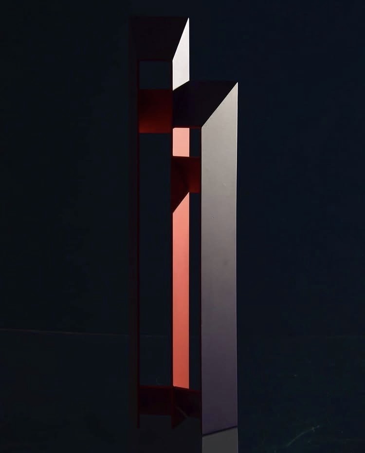 Escultura vertical de la serie Personas, en rojo y blanco, sobre fondo oscuro