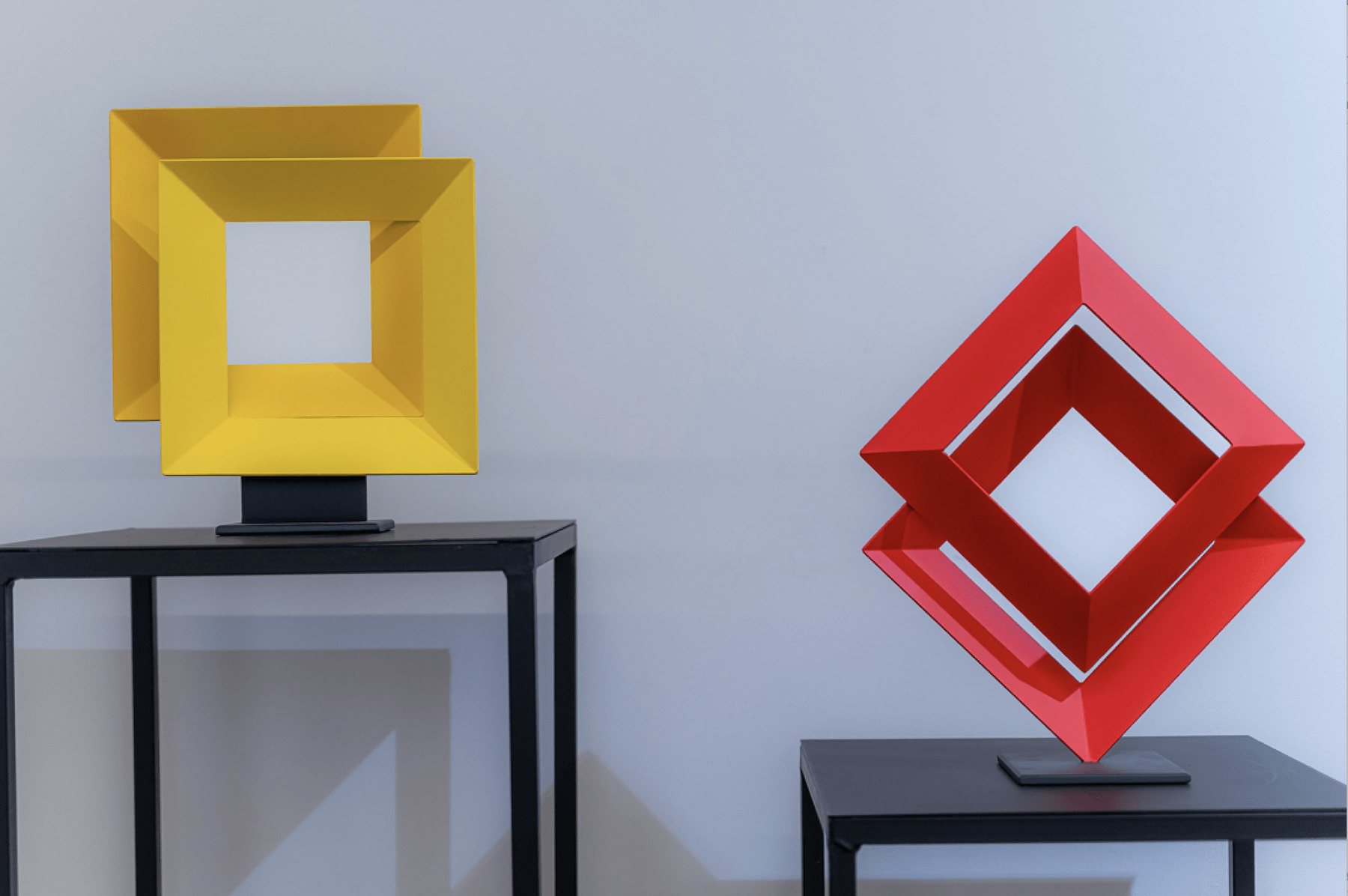 Dos esculturas de marcos entrelazados, en amarillo y en rojo, sobre mesas auxiliares