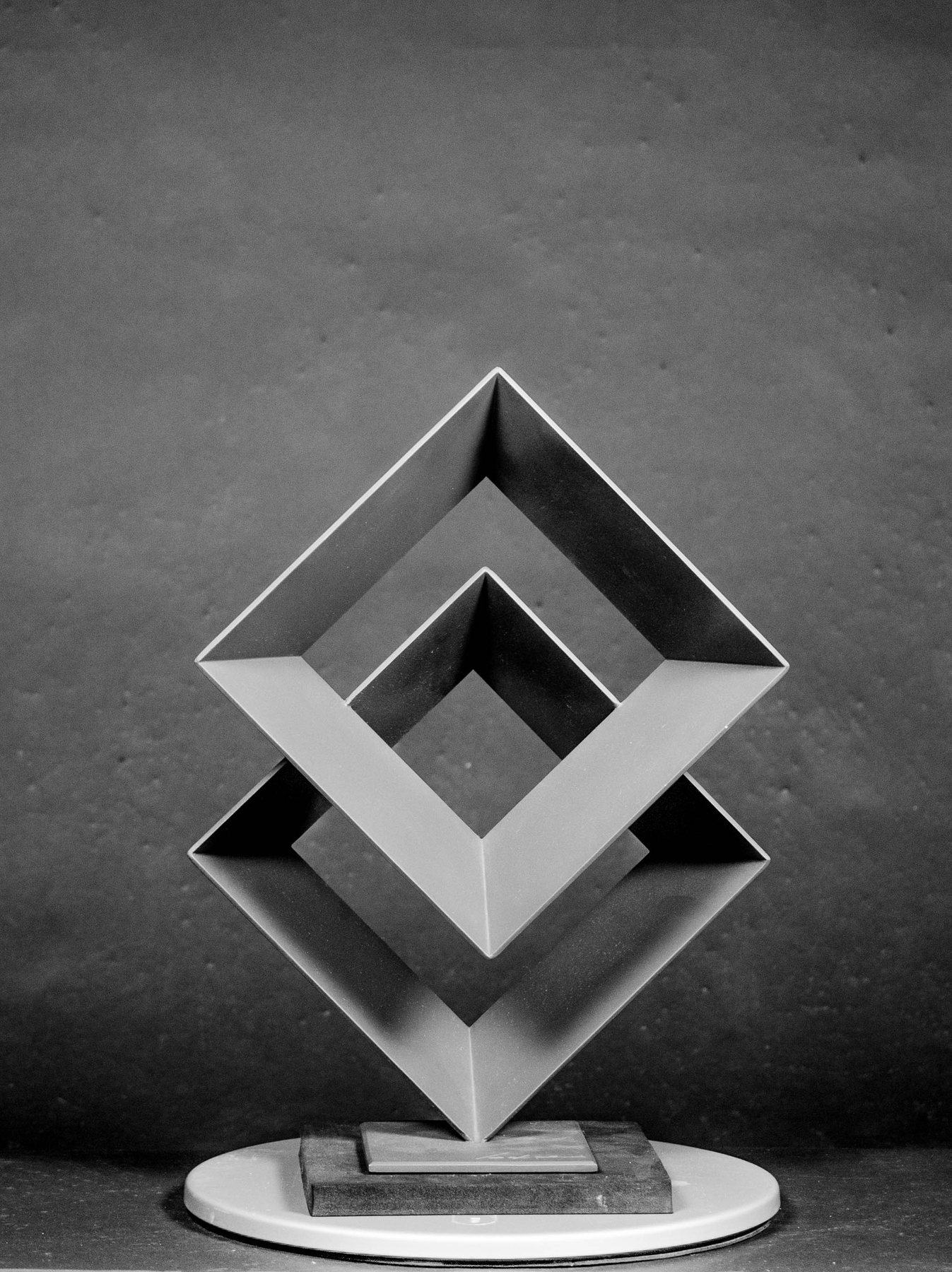 Escultura de marco geométrico en gris, sobre pedestal